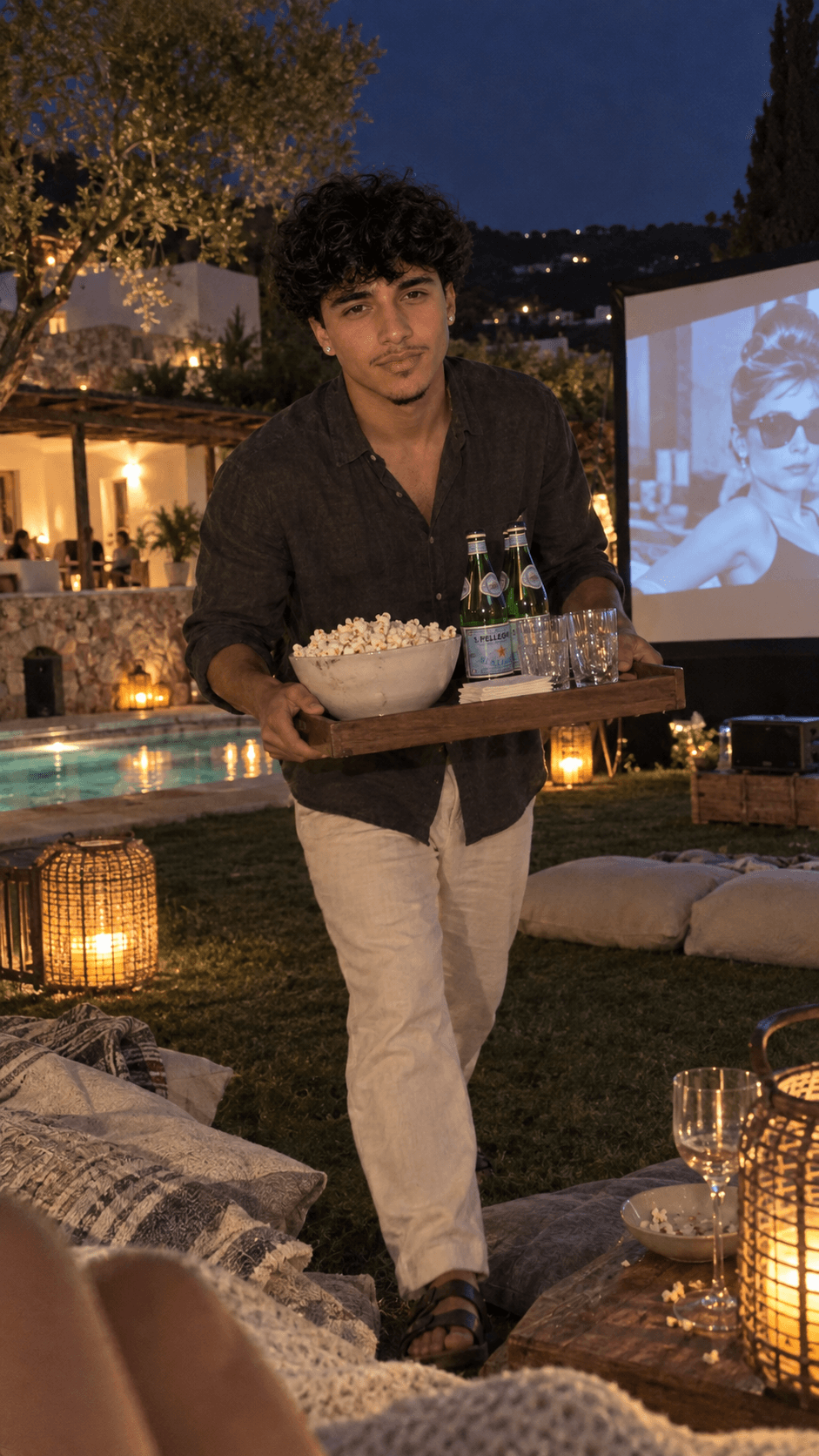 AI-generated man carrying popcorn and sparkling water across a lantern-lit villa lawn for an outdoor movie